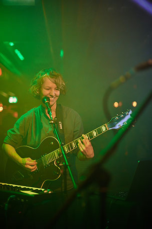 Die Künstlerin Inga (Trikont Label) steht Lächeln mit ihrer Gitarre auf der Bühne, Konzertfotografie, © Florian Freund