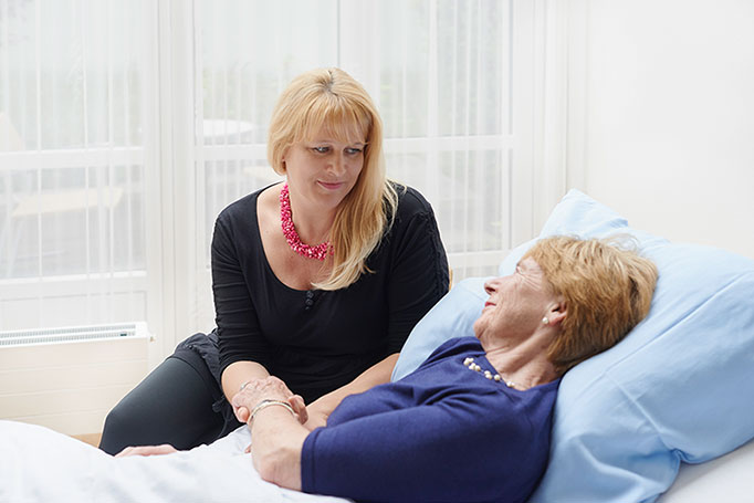 palliative Betreuung durch eine eherenamtliche Mitarbeiterin, die am Bett einer Patientin sitzt